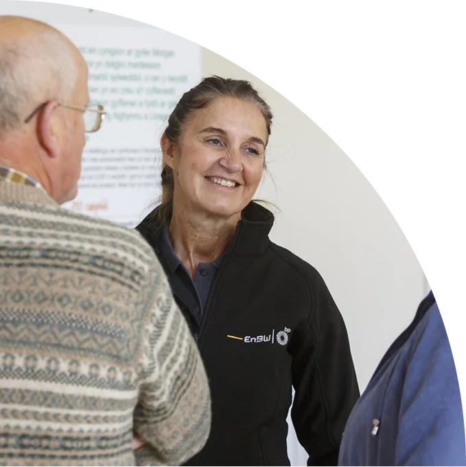 Woman in black EnBW jacket smiling and talking to two people indoors